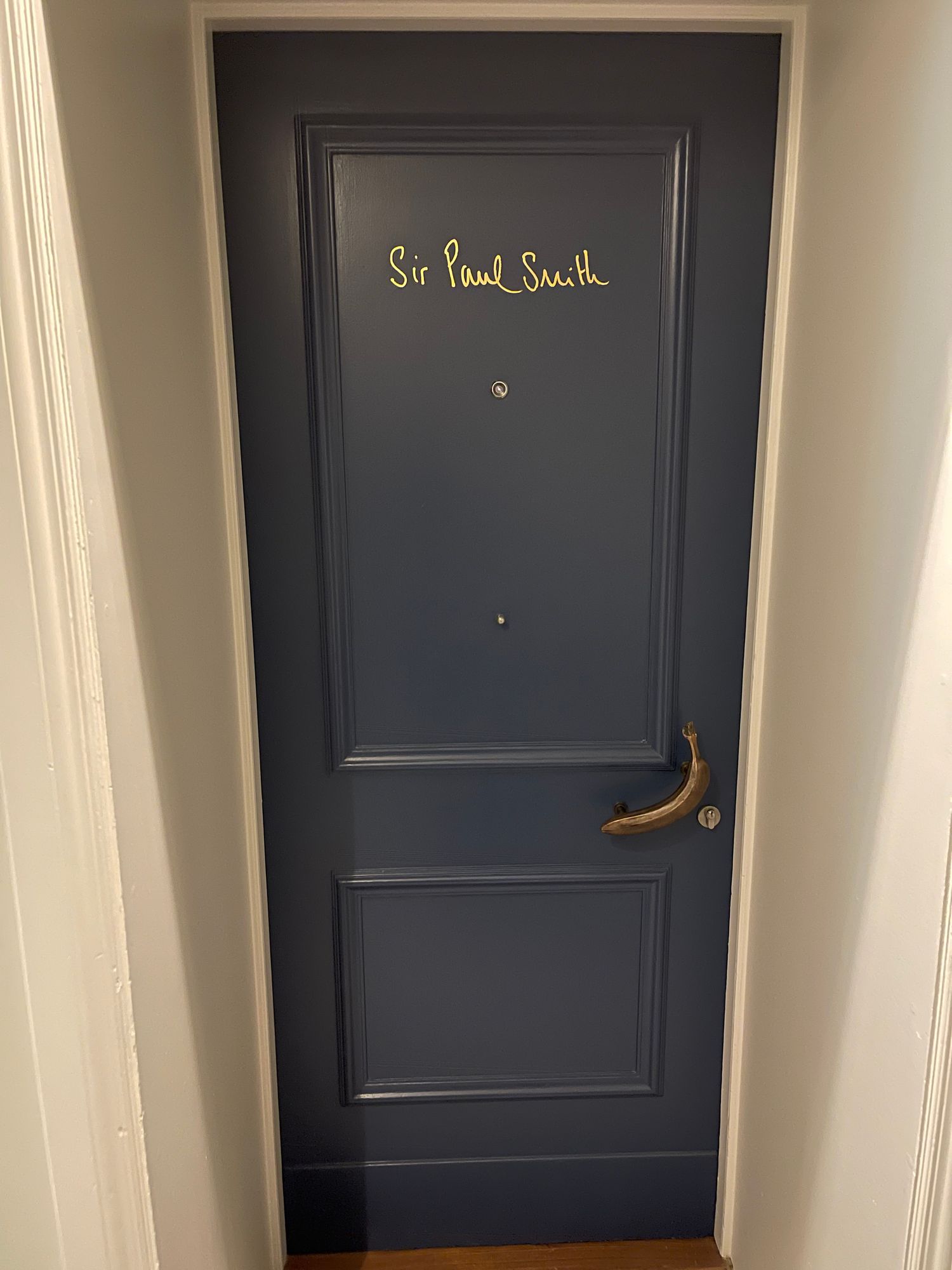 Navy-painted guest-room door at Brown's Hotel, Mayfair, lettered 'Sir Paul Smith' in gold, with a brass lever handle.